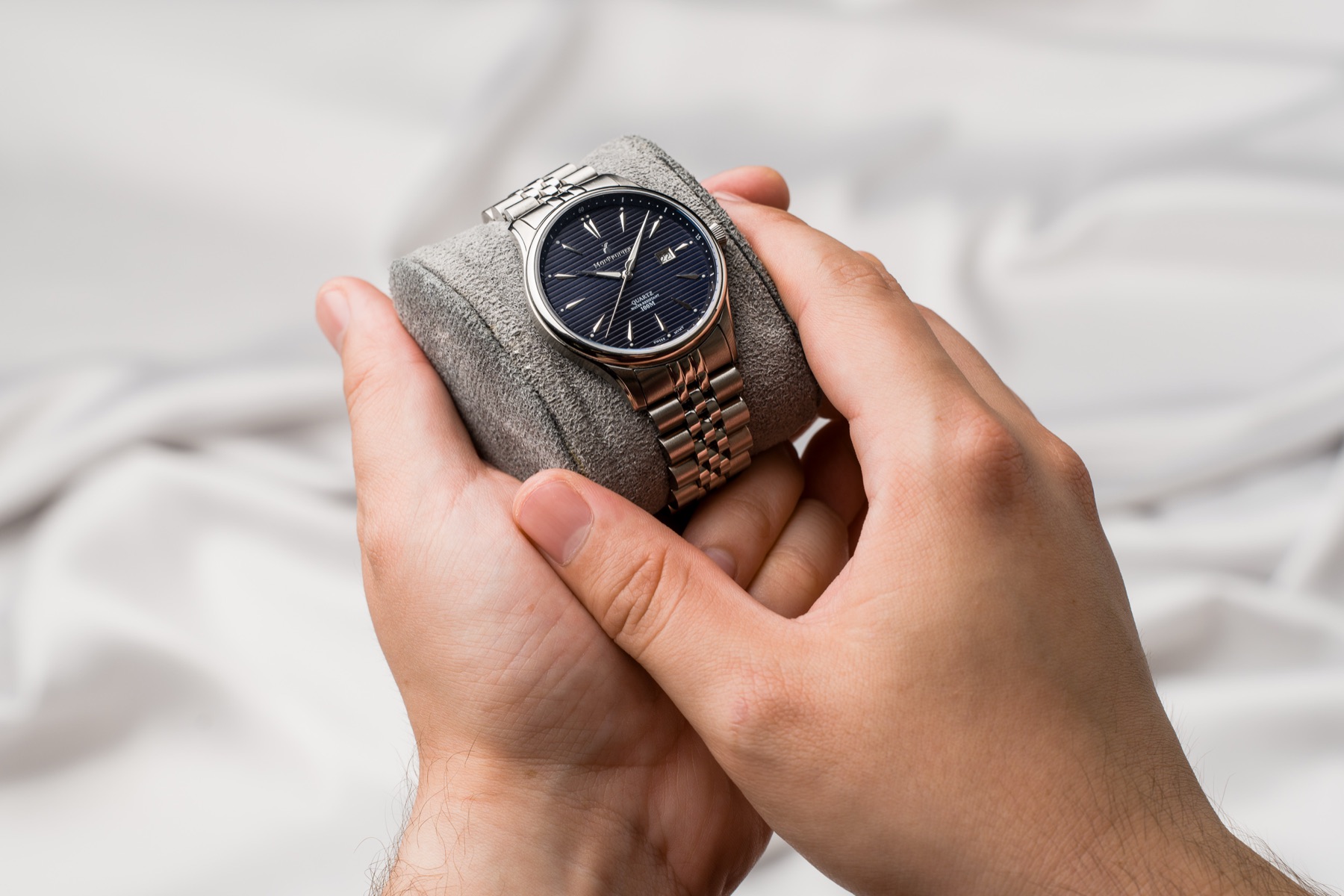 Deep Blue watch held in two hands on a grey cushion